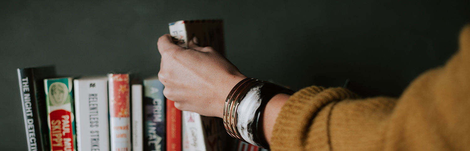 a hand picking up a book from a row of books