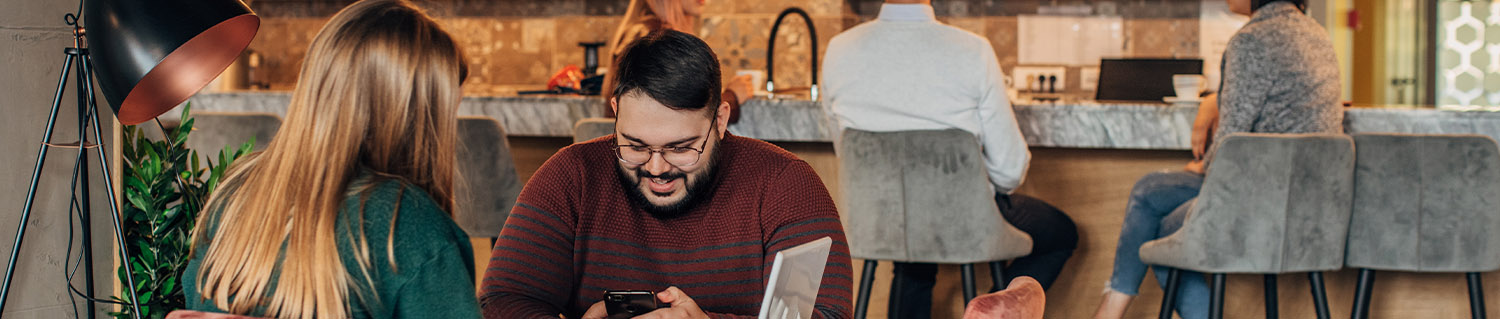 man holding a phone sitting with a woman at a table with a laptop