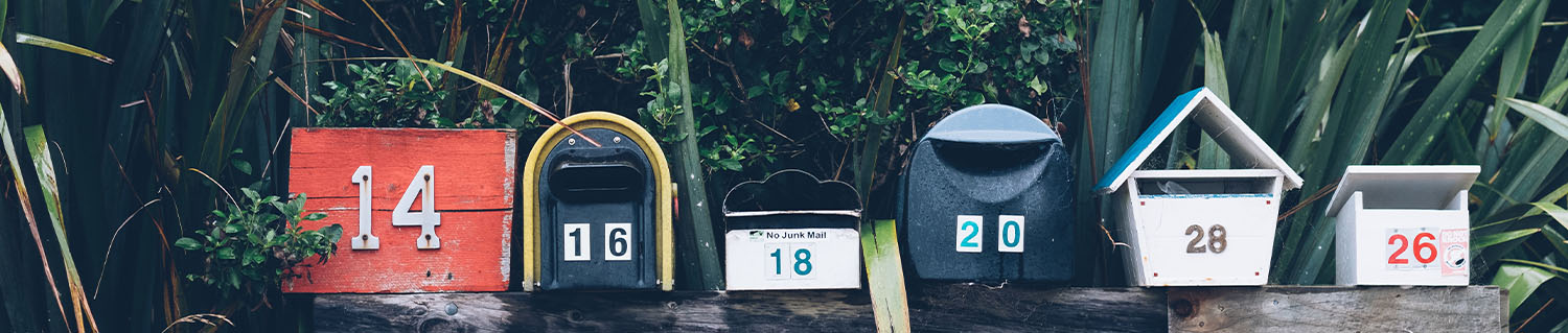 six mailboxes of various shapes lined up side by side